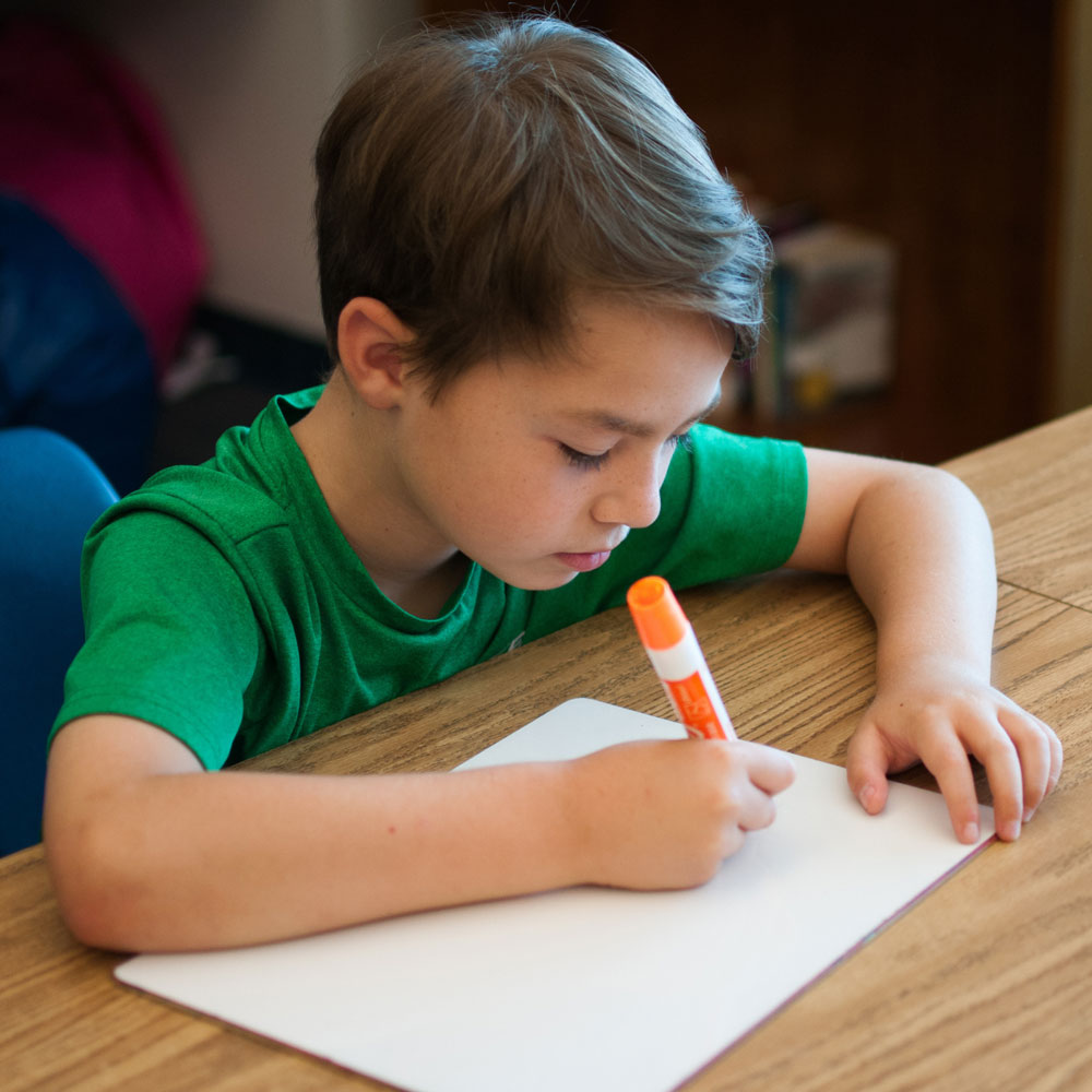 Student sitting at desk writing on a whiteboard